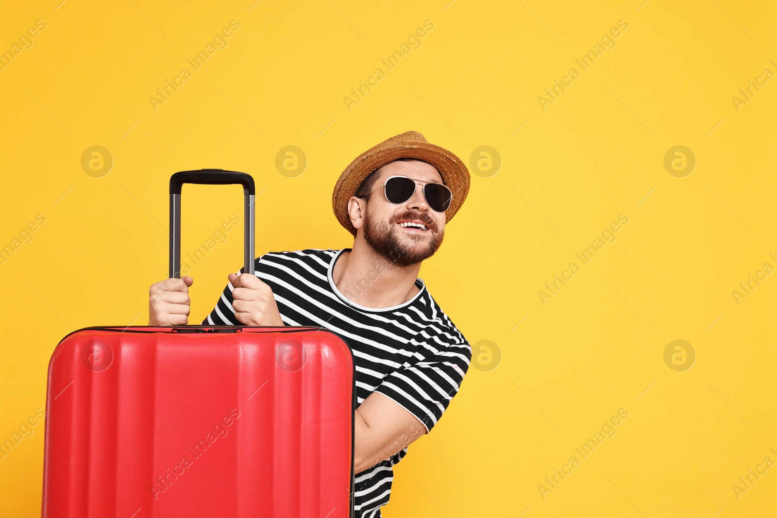 Photo of Happy man in sunglasses with suitcase on orange background, space for text