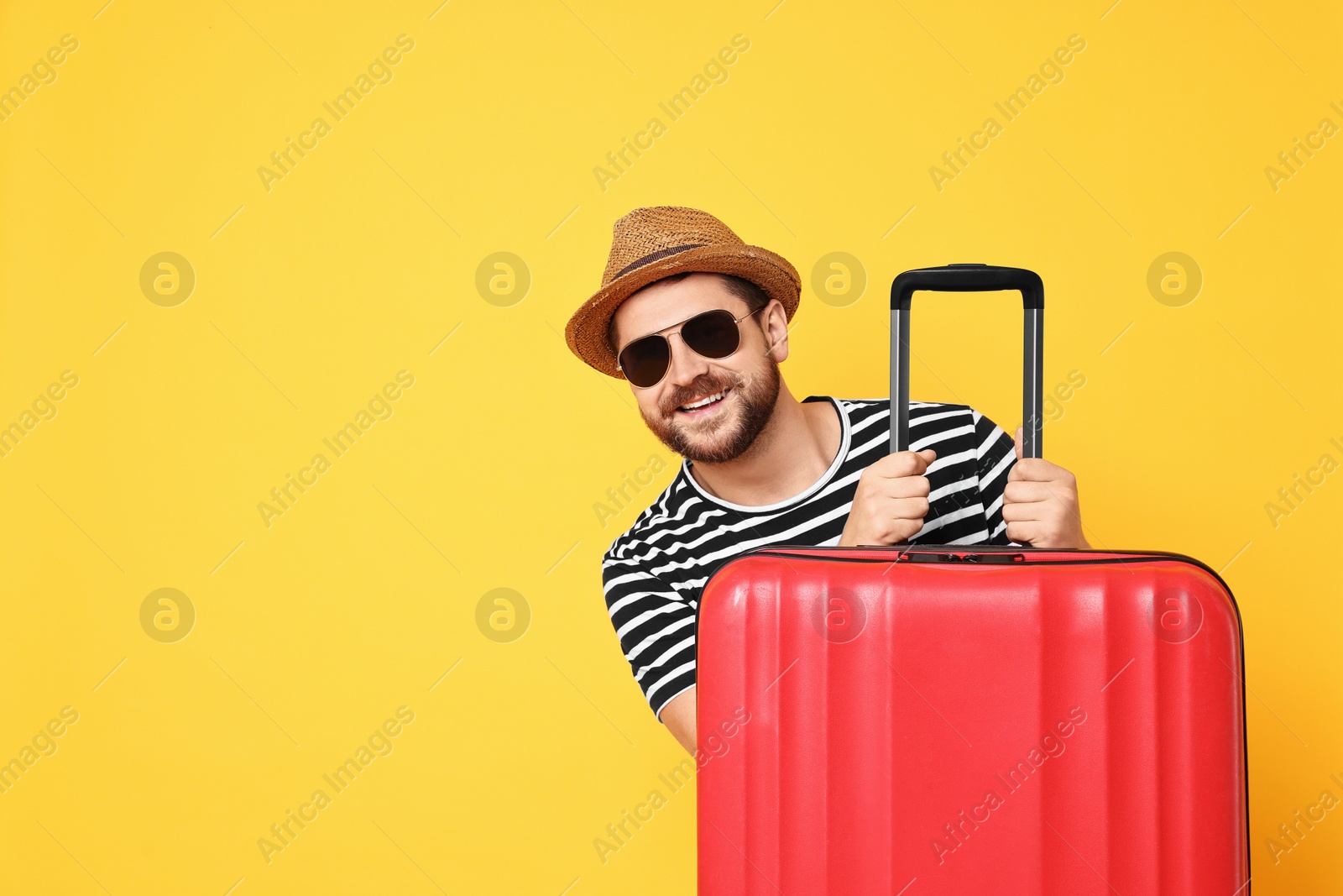 Photo of Happy man in sunglasses with suitcase on orange background, space for text