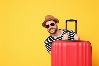 Photo of Happy man in sunglasses with suitcase on orange background, space for text