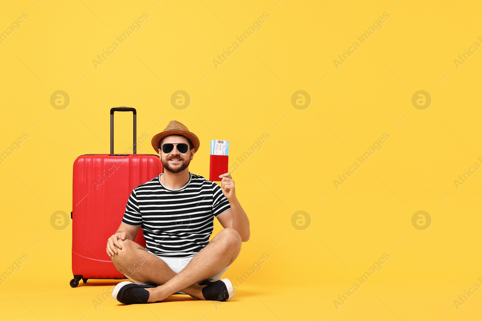 Photo of Happy man in sunglasses with passport, tickets and suitcase on orange background, space for text