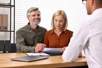 Pension plan. Couple consulting with insurance agent at table indoors