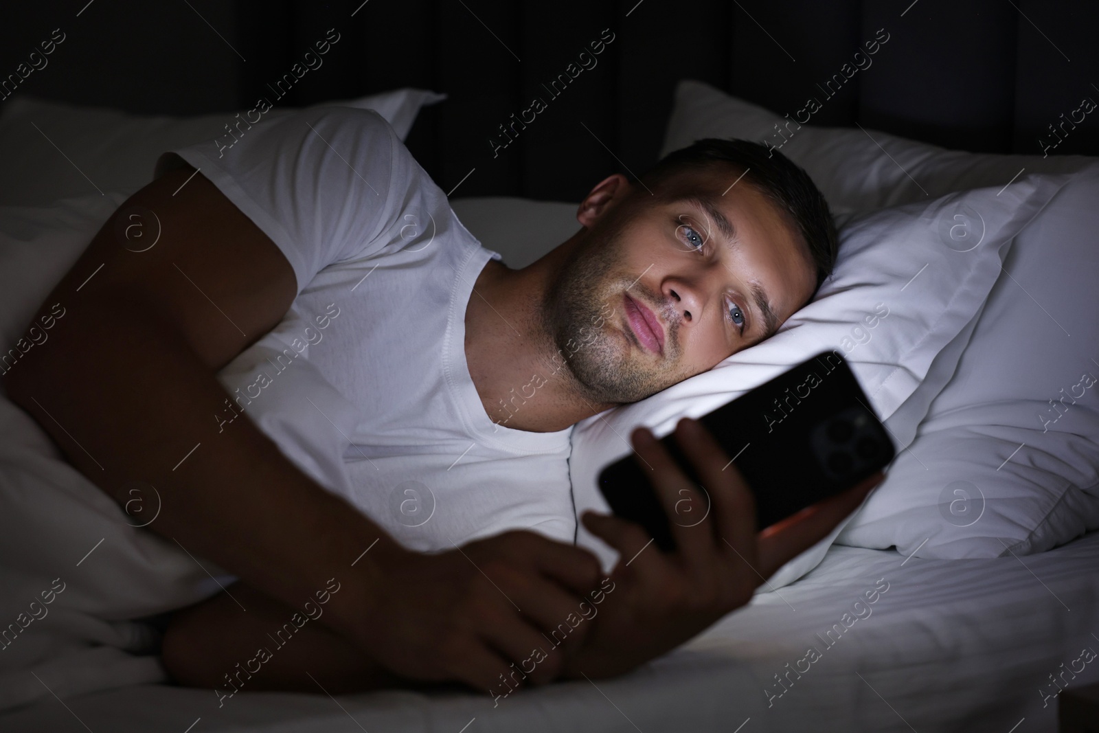 Photo of Bad habit. Man using smartphone in bed at night