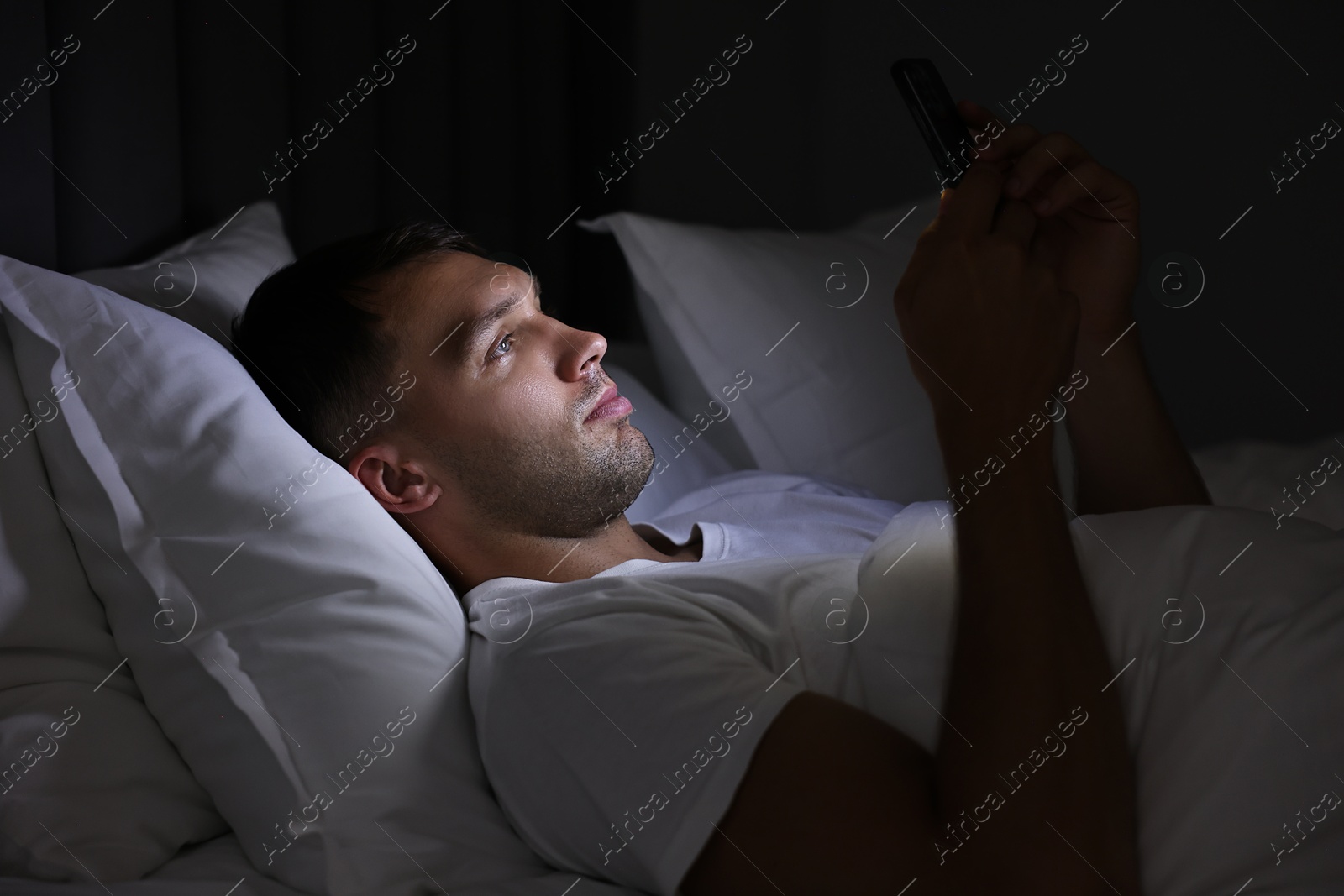 Photo of Bad habit. Man using smartphone in bed at night