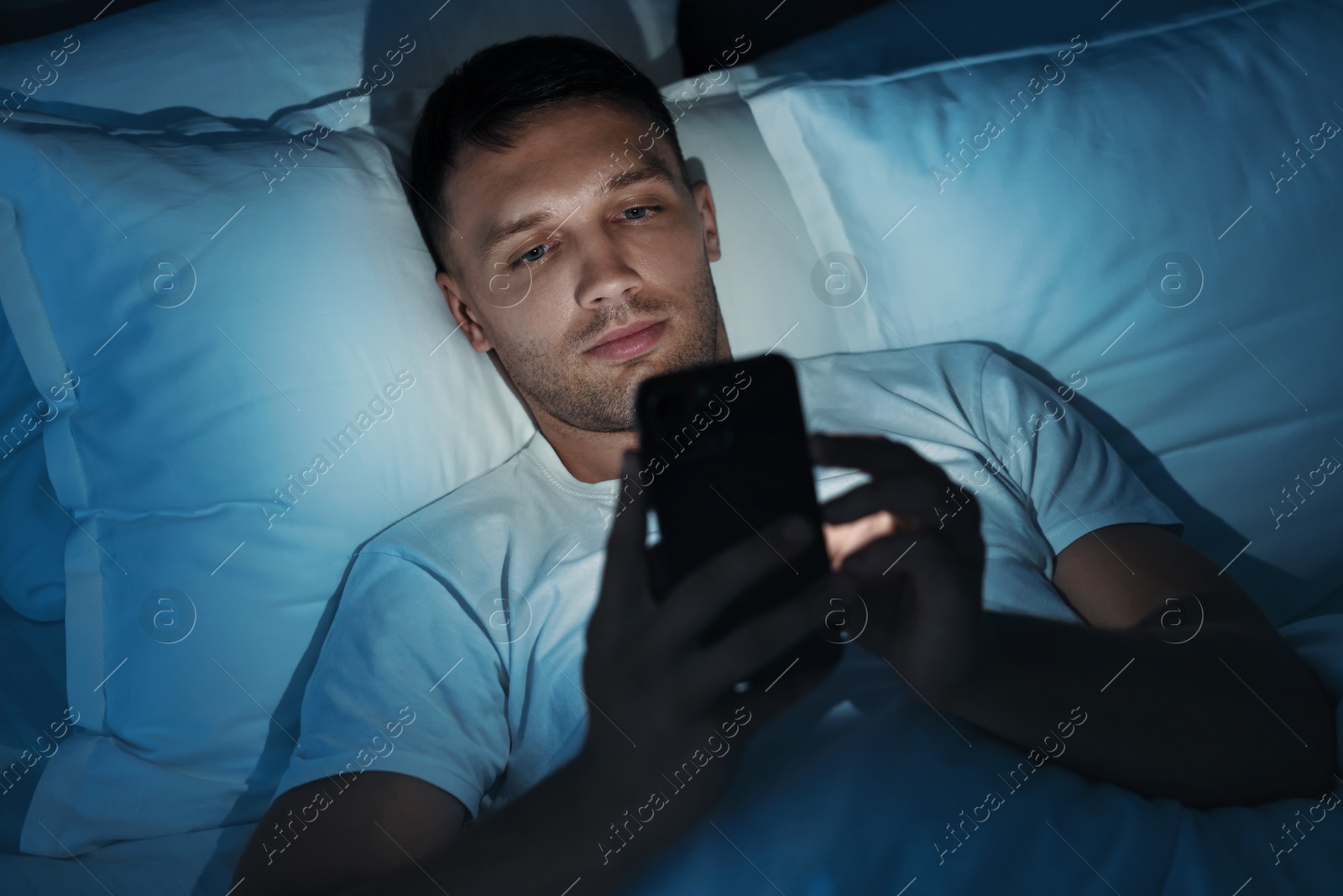 Photo of Bad habit. Man using smartphone in bed at night