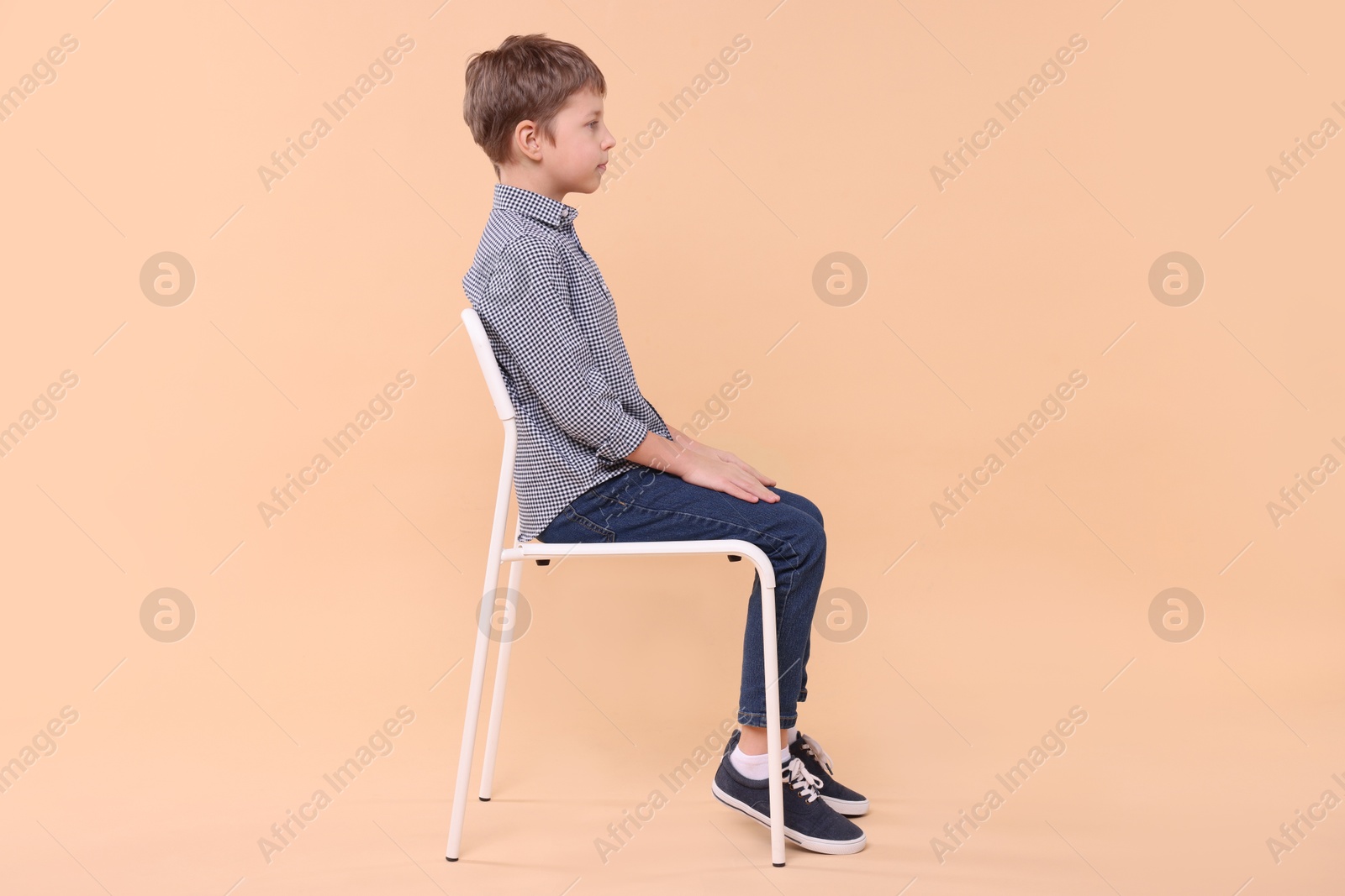 Photo of Boy with correct posture sitting on chair against beige background