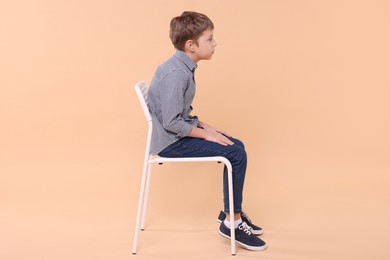 Boy with incorrect posture sitting on chair against beige background