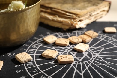 Photo of Wooden runes, old book and bowl on divination mat, closeup