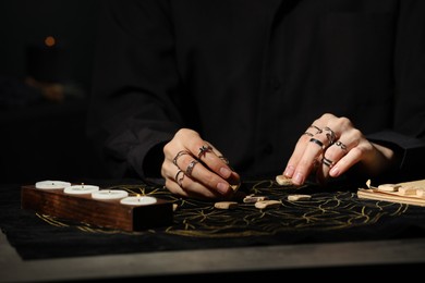 Photo of Woman with wooden runes at dark gray table, closeup