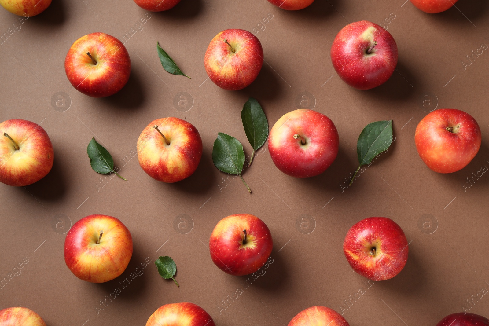 Photo of Ripe red apples and green leaves on brown background, flat lay