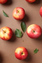 Photo of Ripe red apples and green leaves on brown background, flat lay