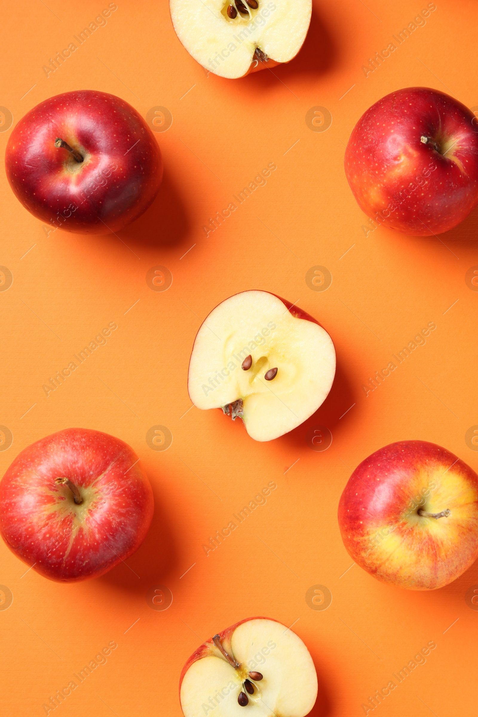 Photo of Whole and cut fresh red apples on orange background, flat lay