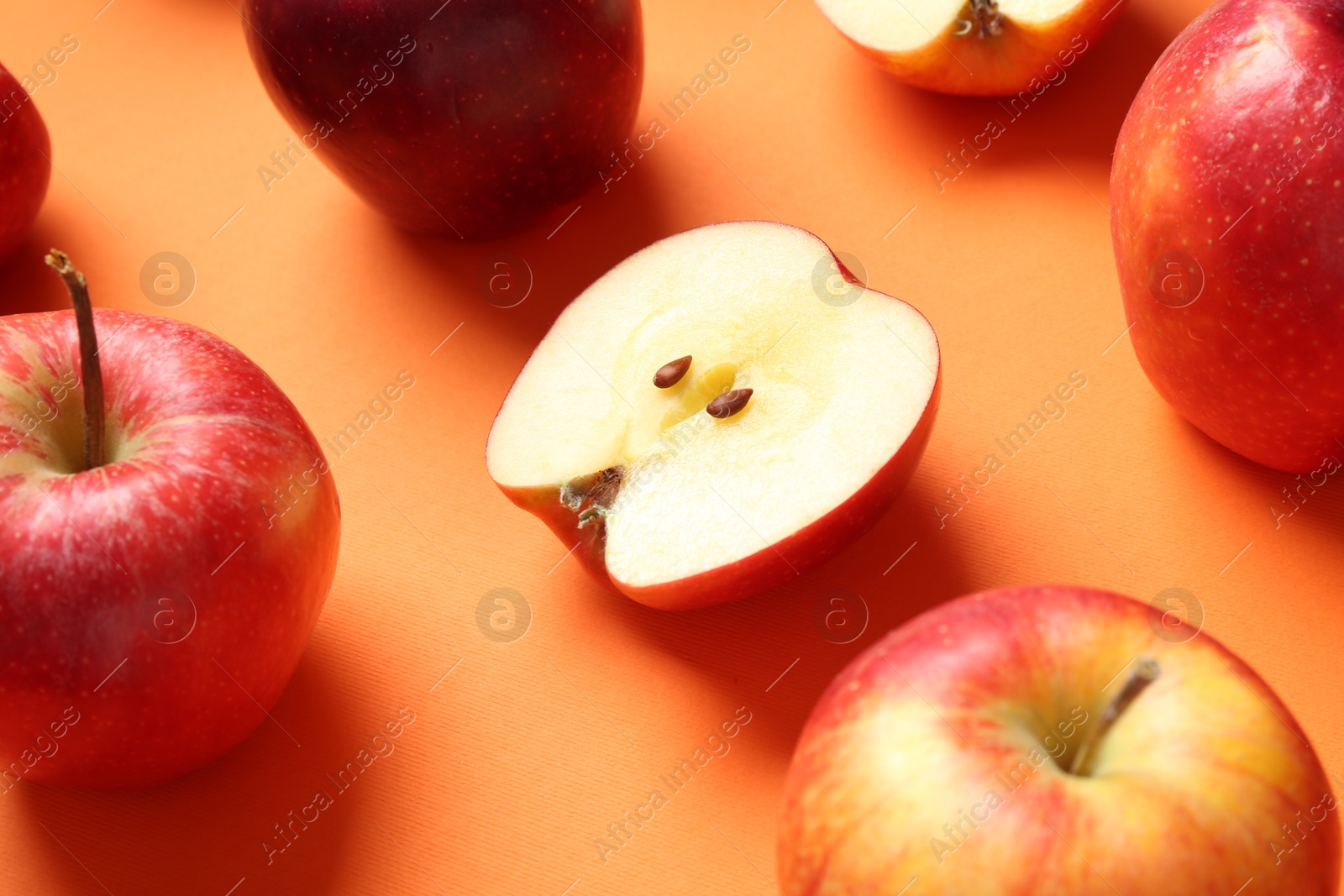 Photo of Whole and cut fresh red apples on orange background, closeup