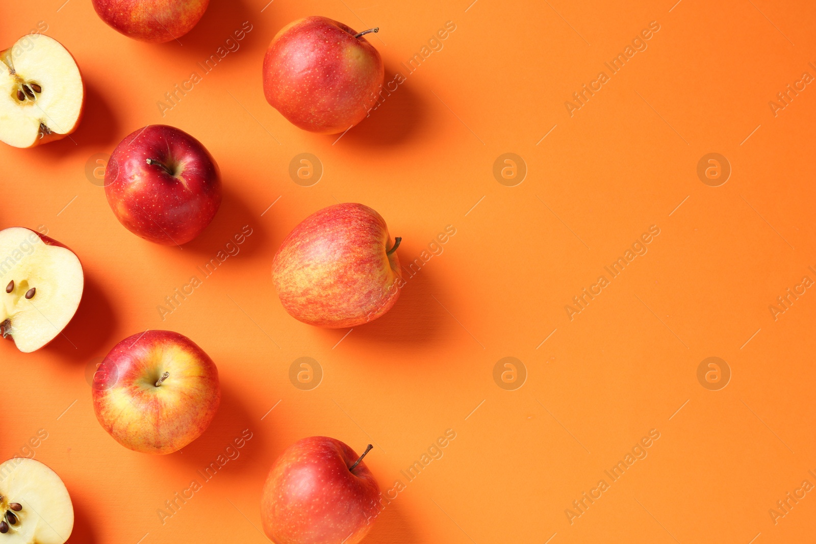 Photo of Whole and cut fresh red apples on orange background, flat lay. Space for text