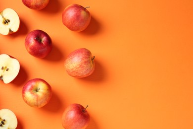 Photo of Whole and cut fresh red apples on orange background, flat lay. Space for text