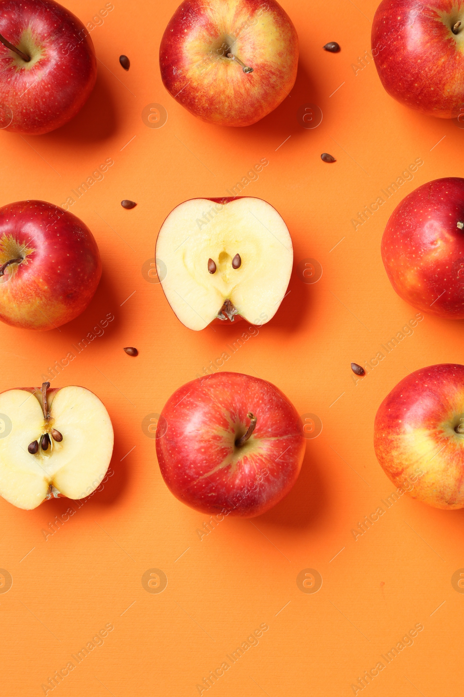 Photo of Fresh red apples and seeds on orange background, flat lay