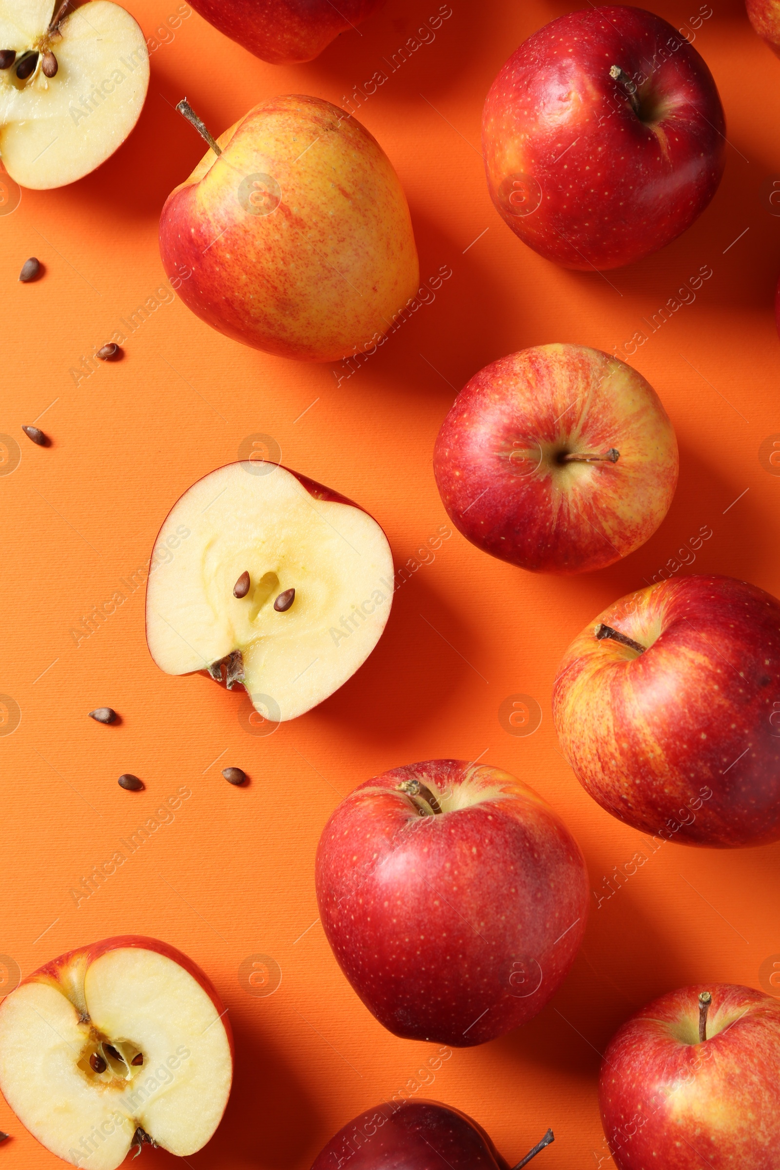 Photo of Fresh red apples and seeds on orange background, flat lay