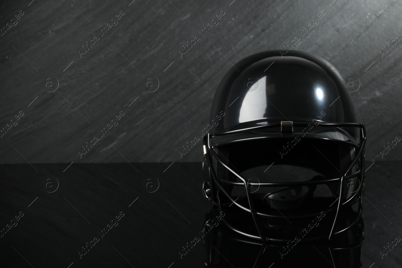 Photo of Black baseball helmet on dark gray background, space for text