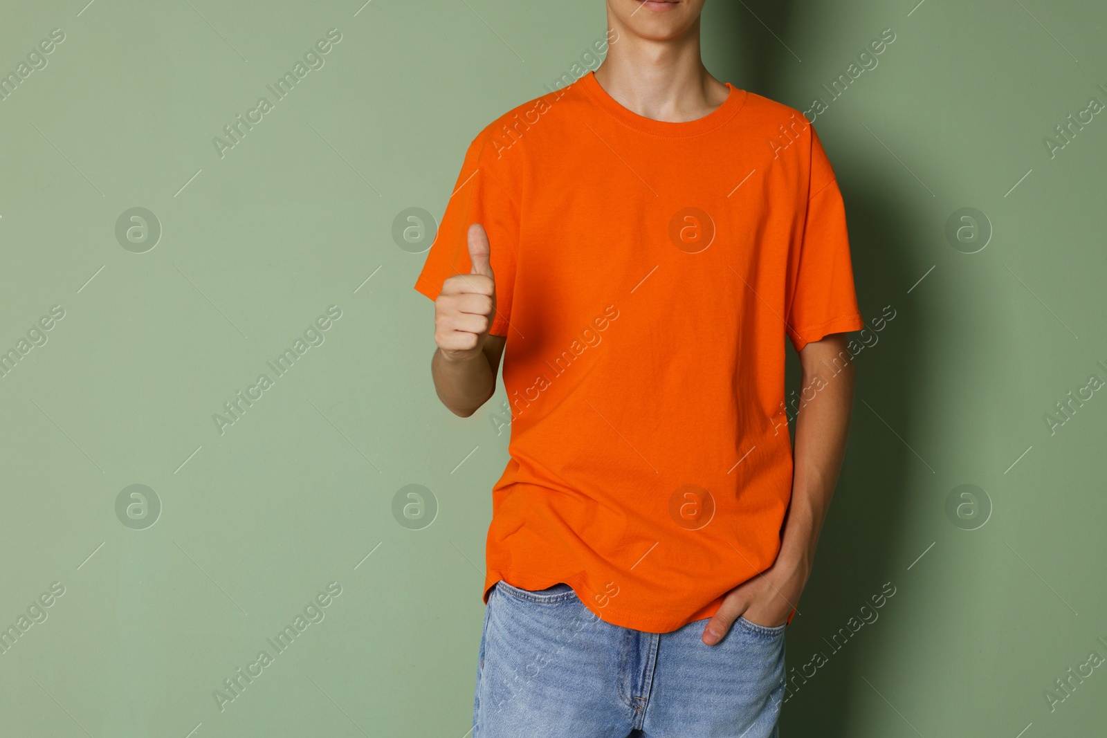 Photo of Teenage boy wearing orange t-shirt and showing thumbs up on green background, closeup. Space for text