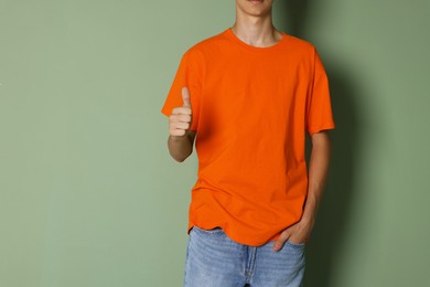 Photo of Teenage boy wearing orange t-shirt and showing thumbs up on green background, closeup. Space for text