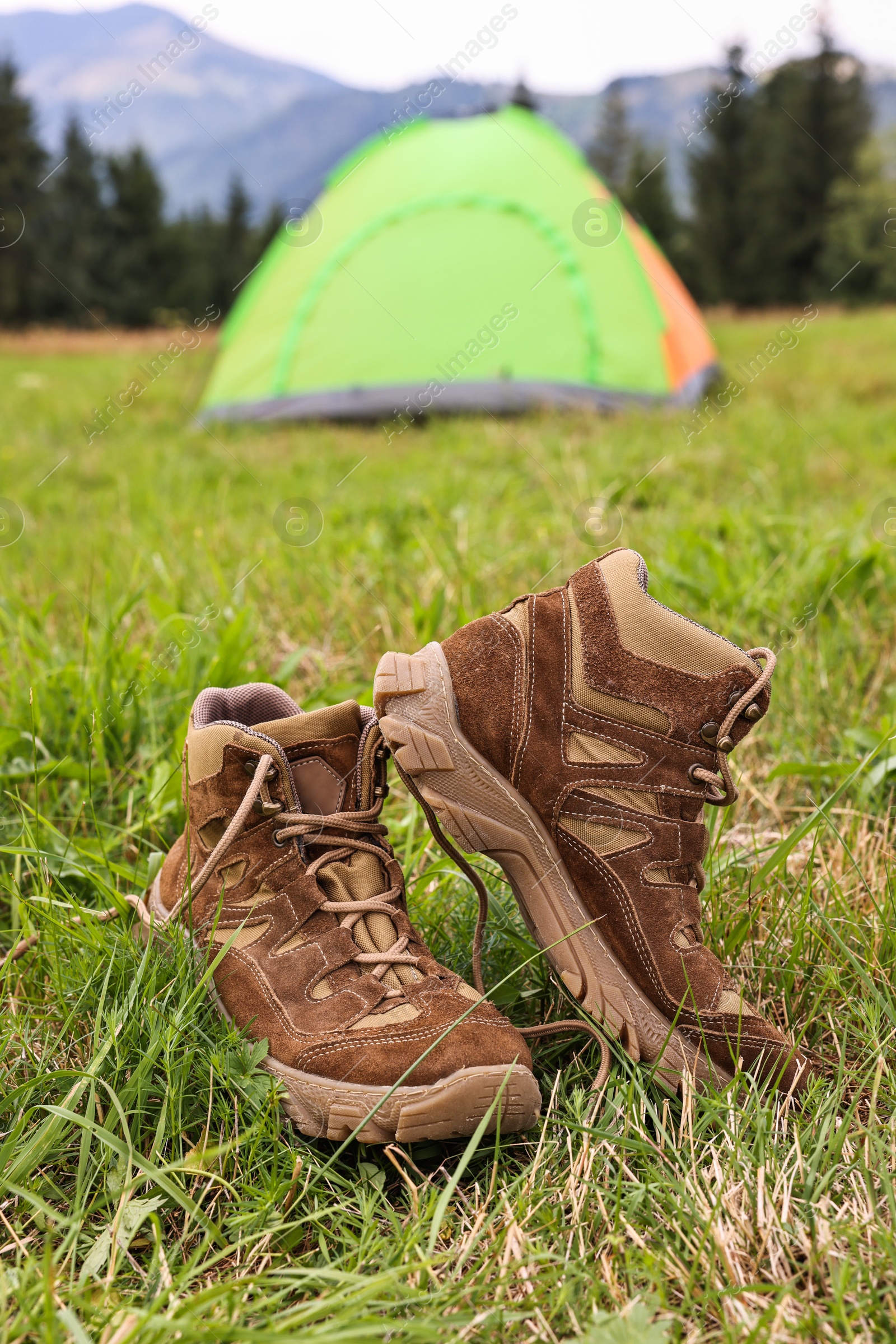 Photo of Trekking shoes and camping tent on green grass outdoors