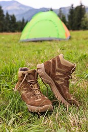 Photo of Trekking shoes and camping tent on green grass outdoors