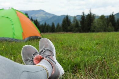 Photo of Woman wearing trekking shoes and lying near tent outdoors, closeup. Space for text