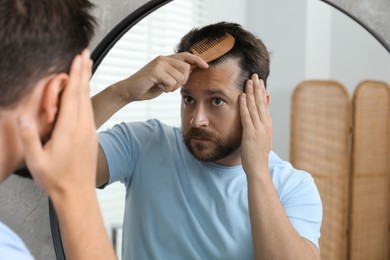 Photo of Man brushing his hair near mirror indoors. Alopecia problem