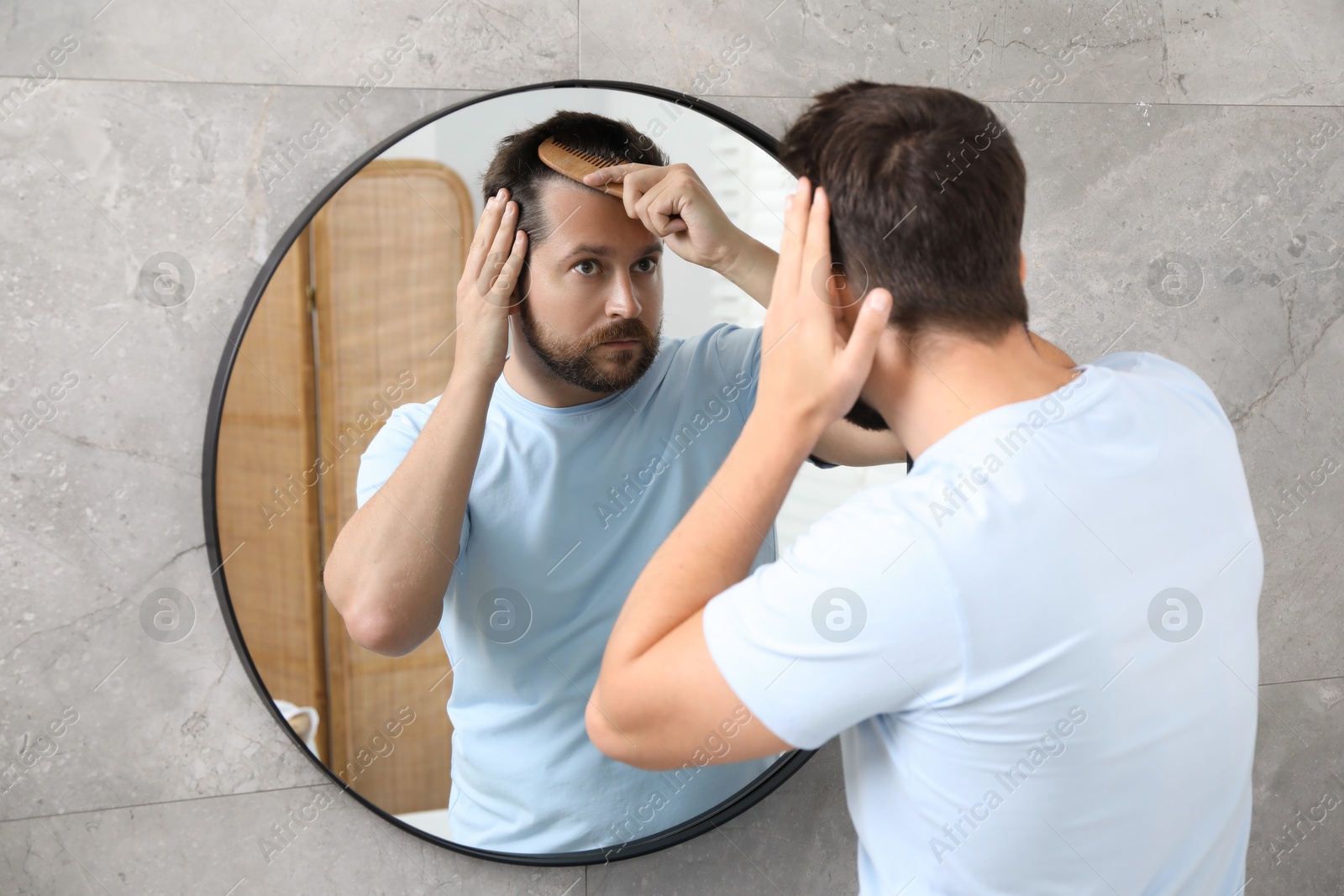 Photo of Man brushing his hair near mirror indoors. Alopecia problem