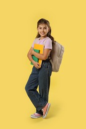 Photo of Girl with backpack and books on yellow background