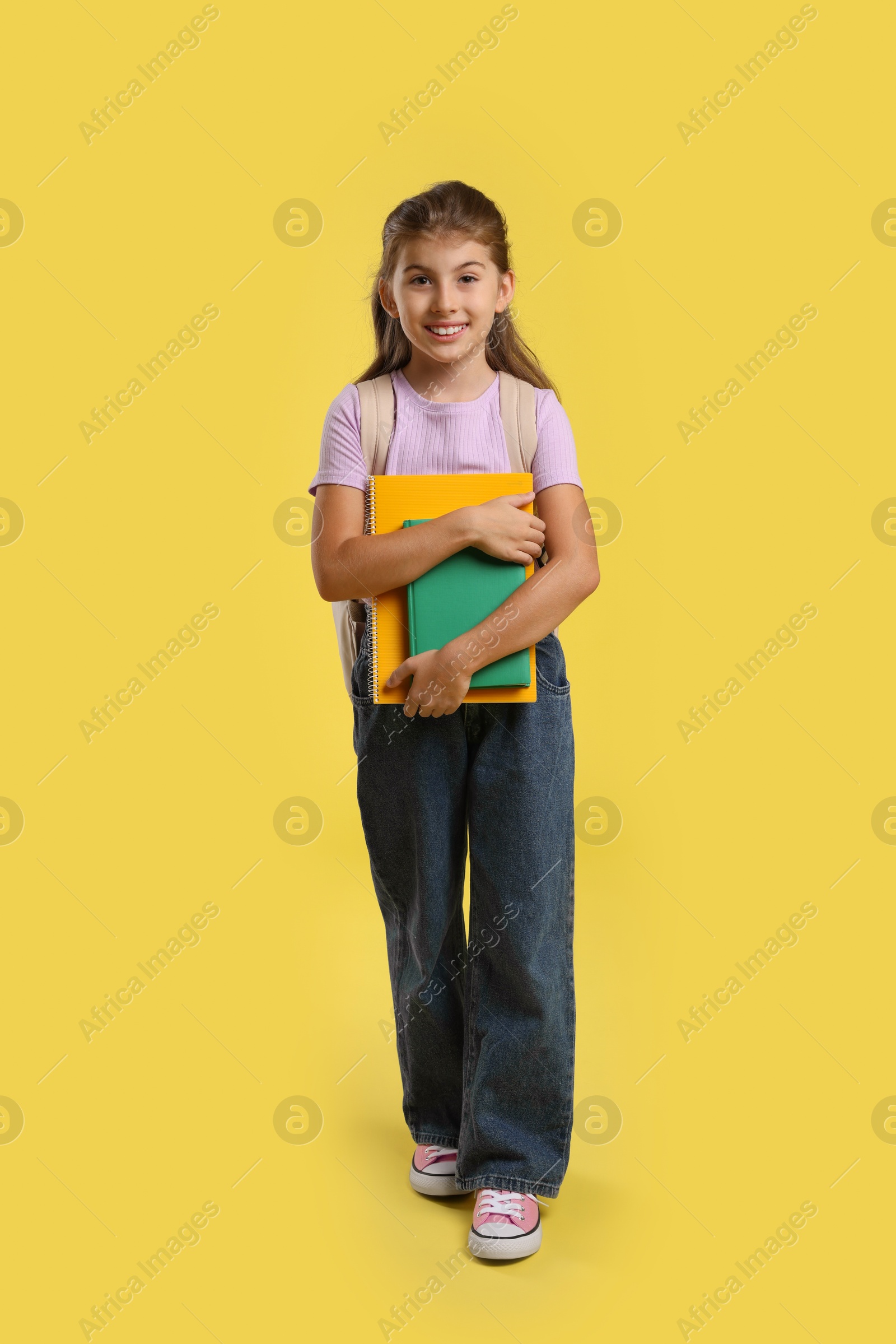 Photo of Girl with backpack and books on yellow background