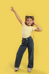 Cute girl listening to music on yellow background