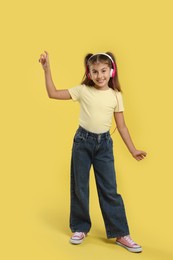 Cute girl listening to music on yellow background