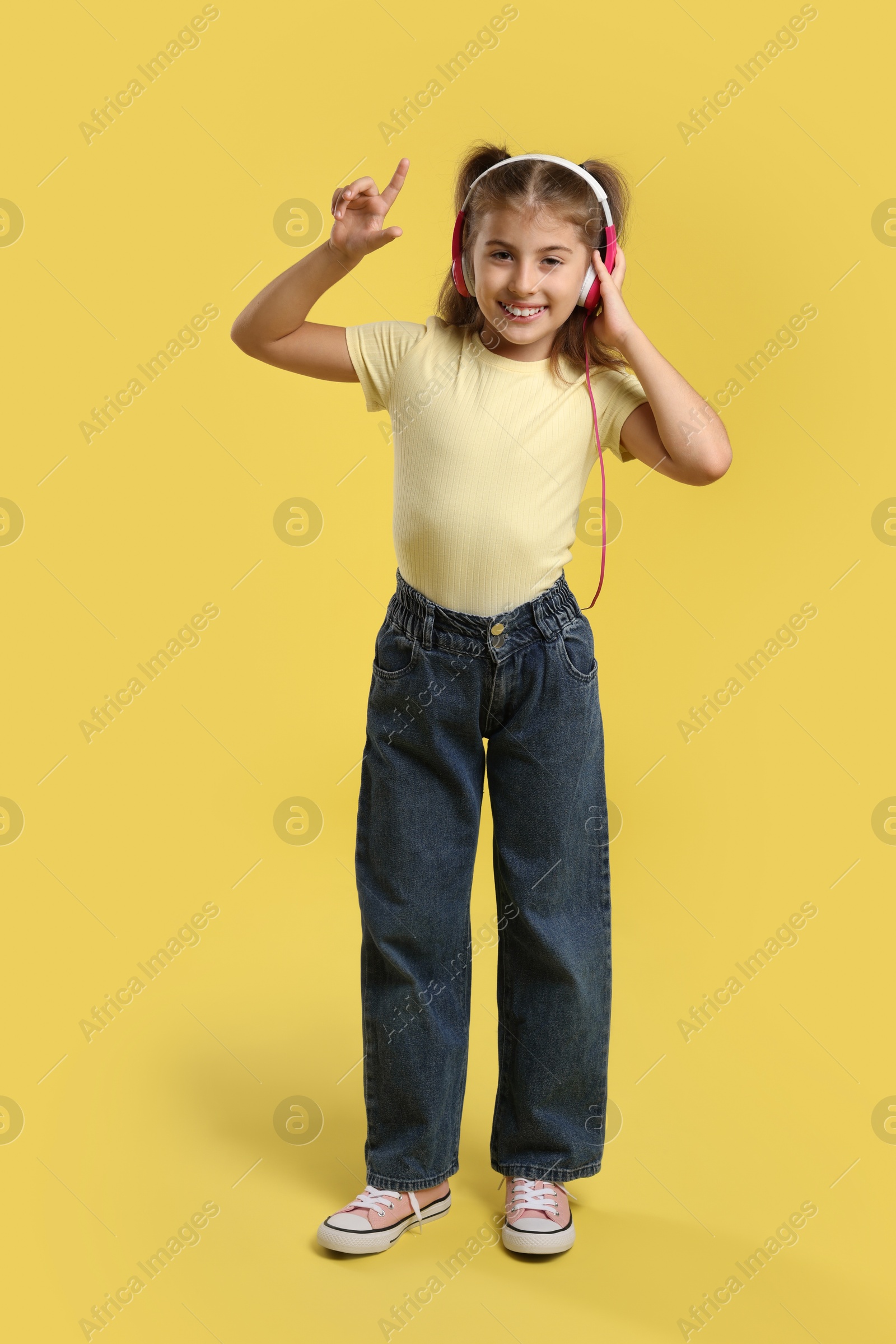 Photo of Cute girl listening to music on yellow background