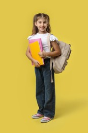 Positive girl with backpack and books on yellow background