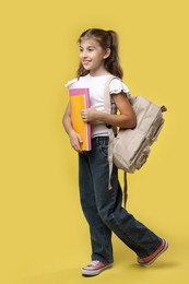 Positive girl with backpack and books on yellow background