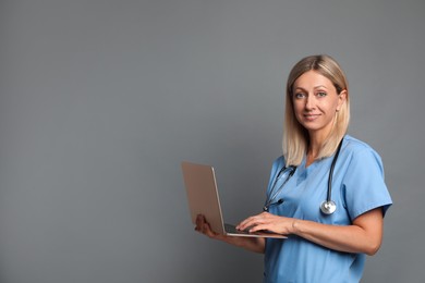 Photo of Doctor in medical uniform with stethoscope using laptop on grey background, space for text