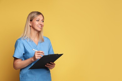 Portrait of nurse in medical uniform with clipboard on yellow background, space for text