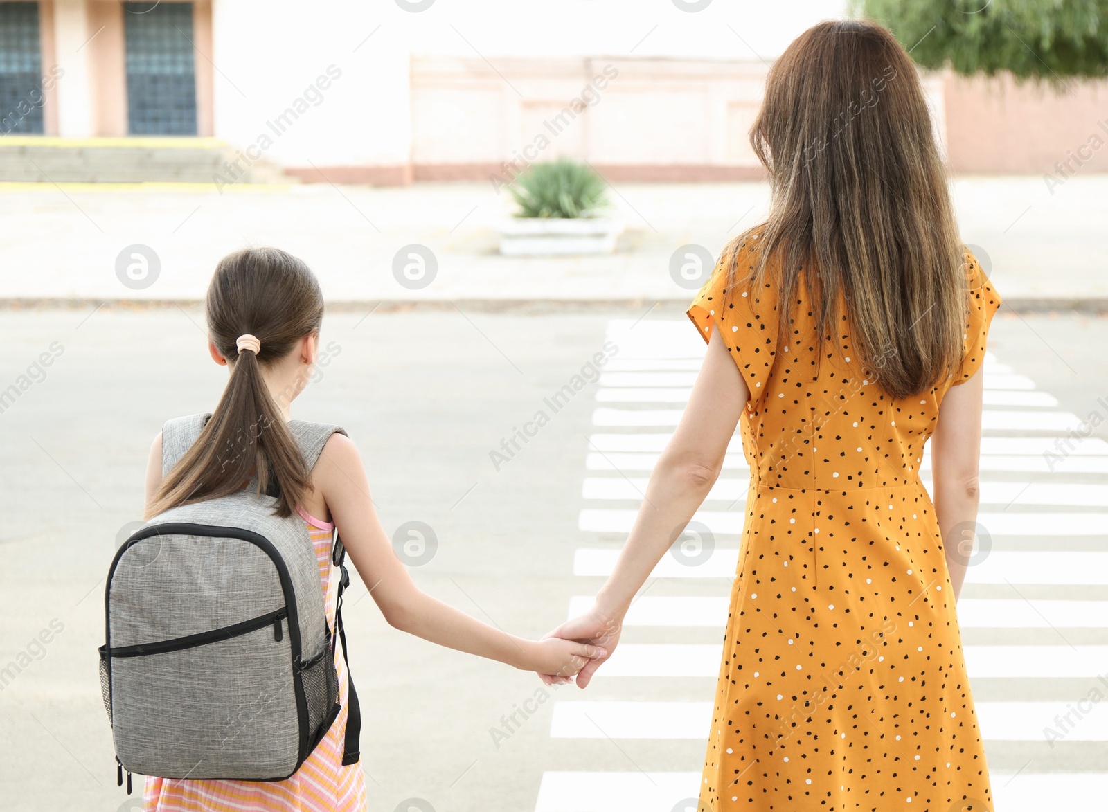 Photo of Mother and daughter holding hands outdoors, back view