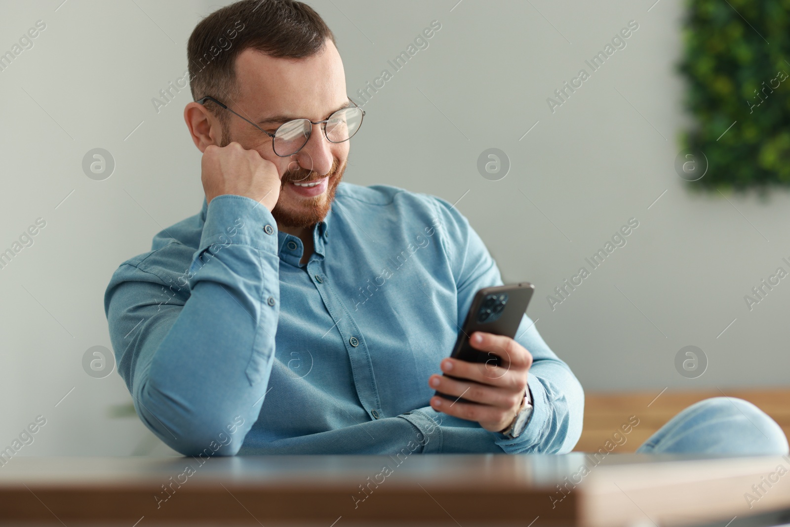 Photo of Smiling man looking at smartphone in office