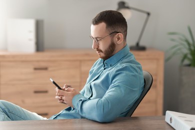 Photo of Handsome man looking at smartphone in office