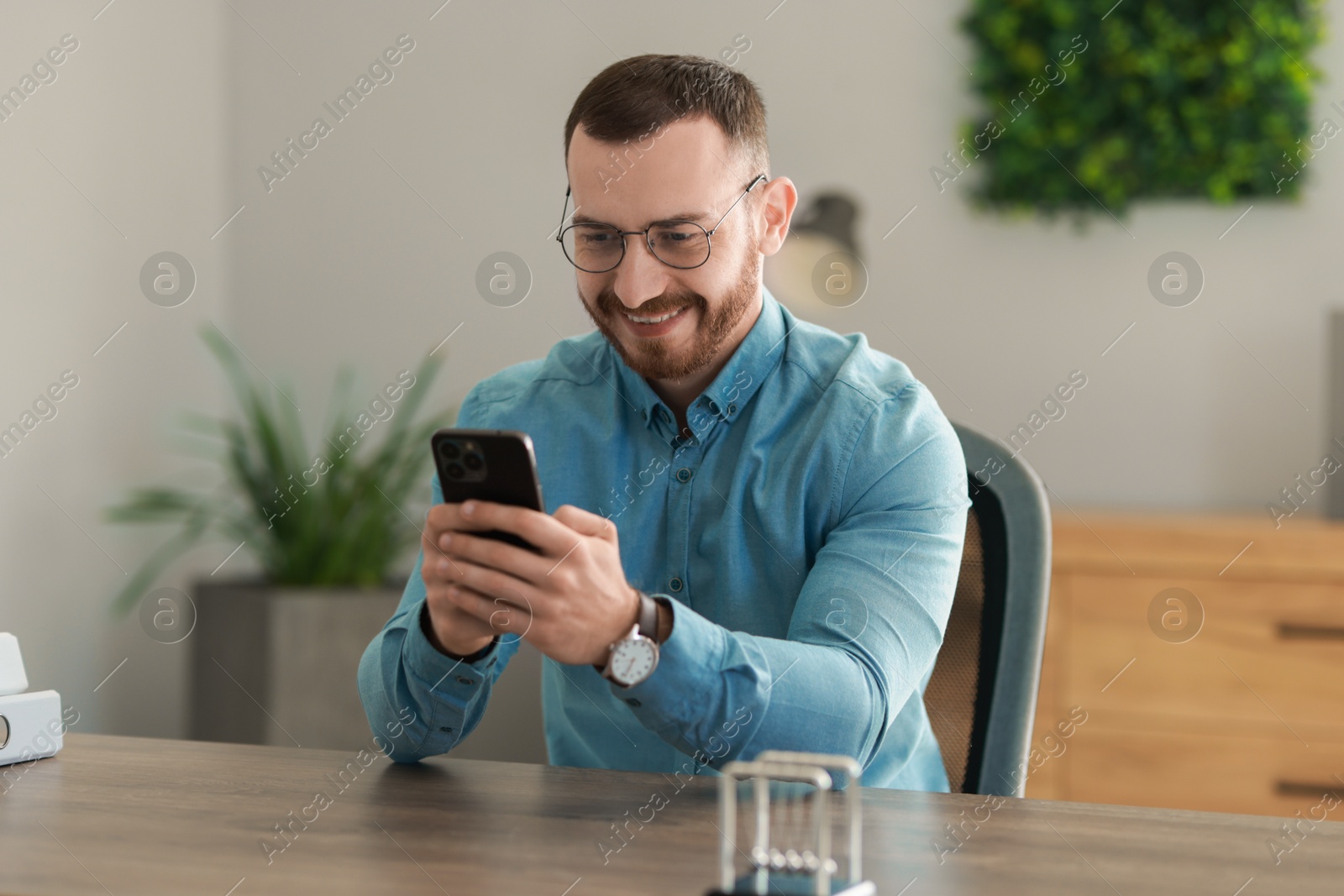 Photo of Smiling man looking at smartphone in office