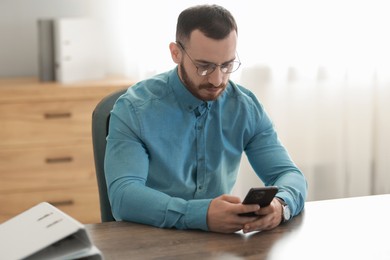 Photo of Handsome man looking at smartphone in office