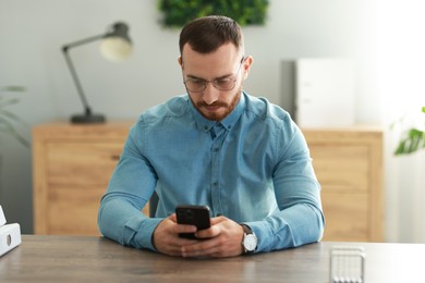 Handsome man looking at smartphone in office