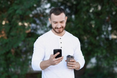 Happy man with paper cup using smartphone on blurred background