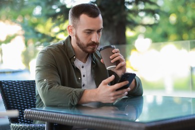 Photo of Handsome man using smartphone and drinking coffee at outdoor cafe