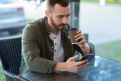 Photo of Handsome man using smartphone and drinking coffee at outdoor cafe