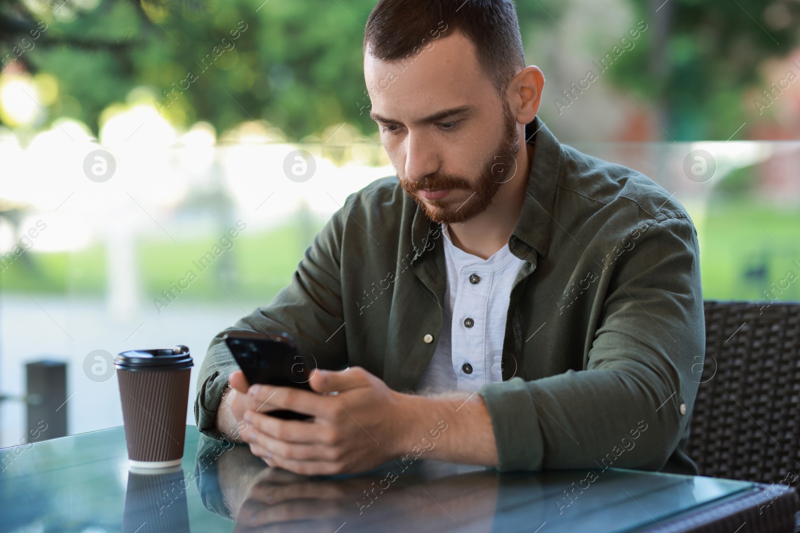 Photo of Handsome man with paper cup using smartphone at outdoor cafe