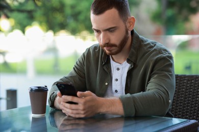 Handsome man with paper cup using smartphone at outdoor cafe