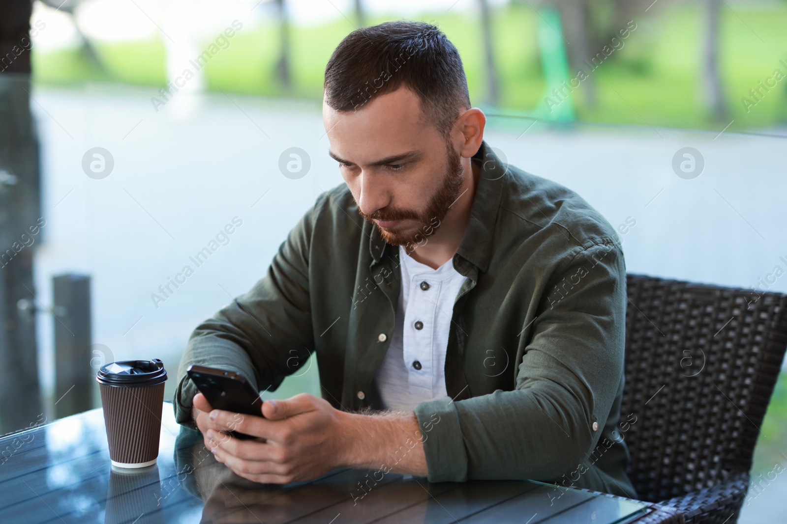 Photo of Handsome man with paper cup using smartphone at outdoor cafe