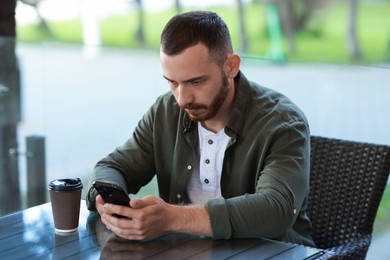 Handsome man with paper cup using smartphone at outdoor cafe